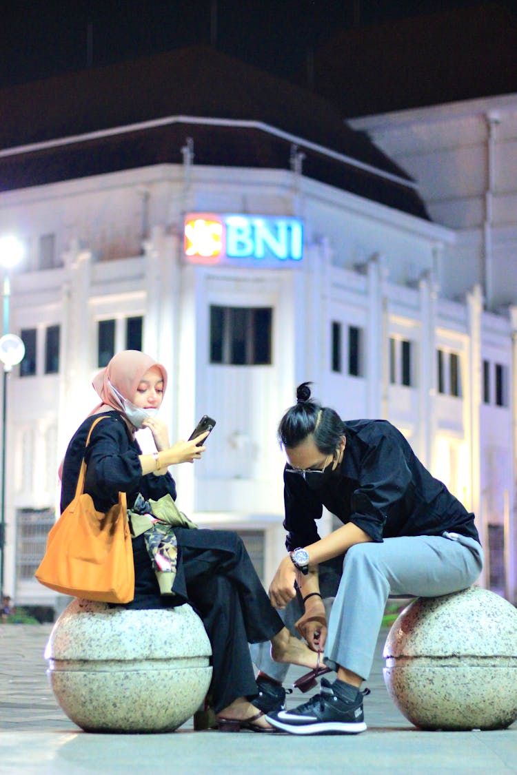 Couple Sitting On Concrete Blocks In Front Of Bank Building