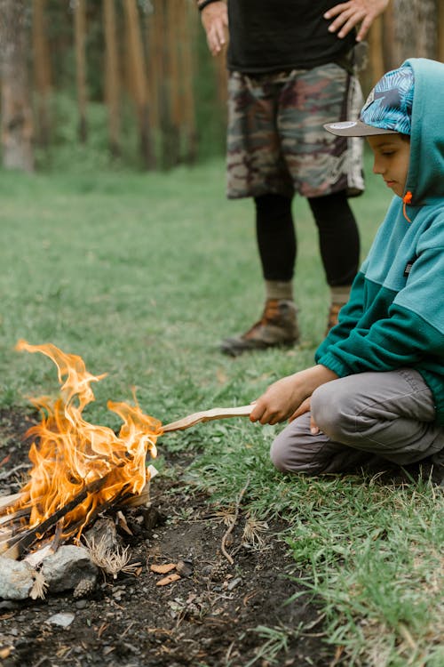 一個穿綠色連帽衫的男孩在篝火上燒一根棍子