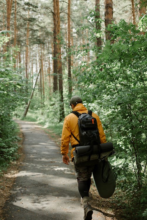 A Person Wearing Yellow Jacket Carrying Black Backpack Walking on Pathway in the Middle of Forrest