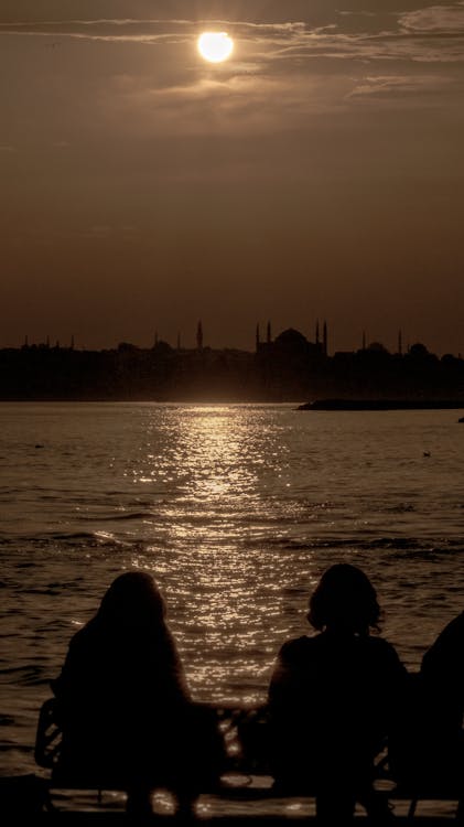 Free Silhouette of Persons Sitting Near Body of Water Stock Photo