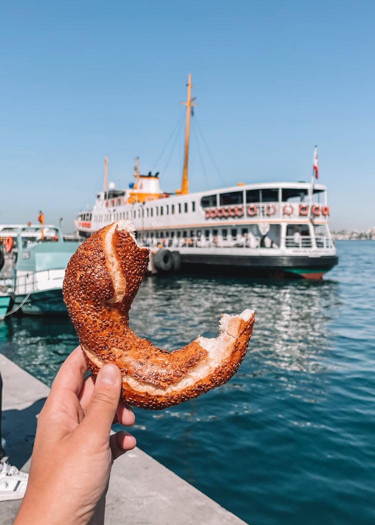 A Person Holding Half Eaten Bread Near A Ship 