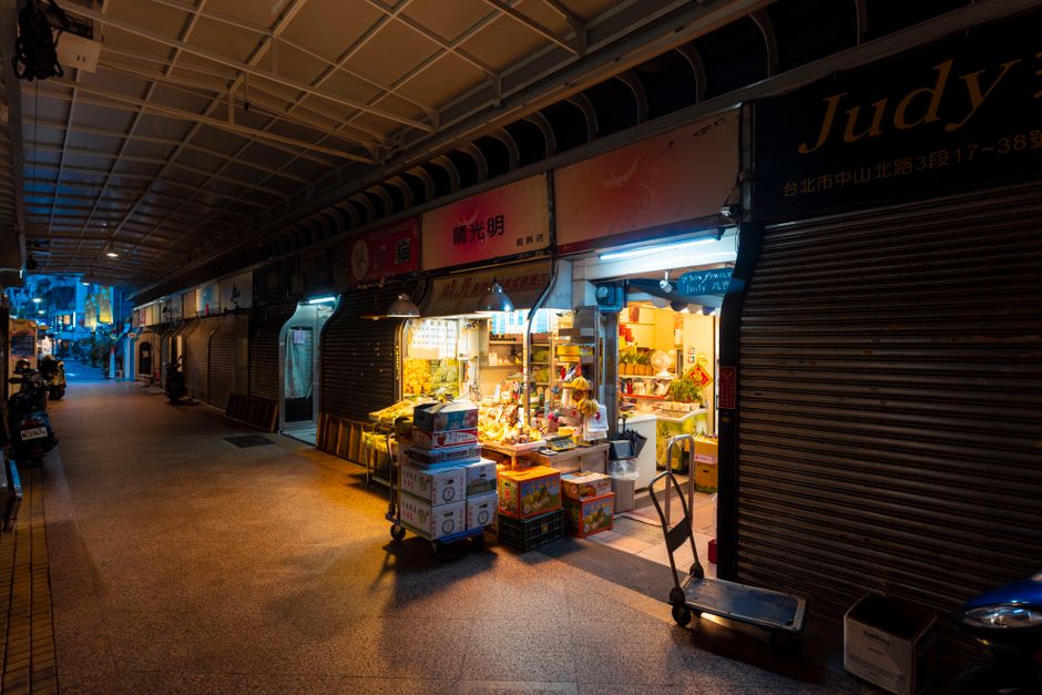 A quiet market alley with a lit fruit stand at dusk.
