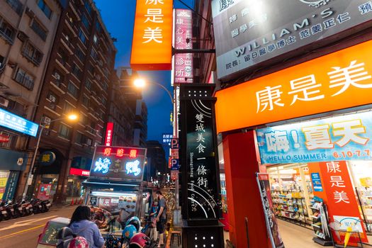 Bustling urban city street with vibrant neon signs and market stalls at night.