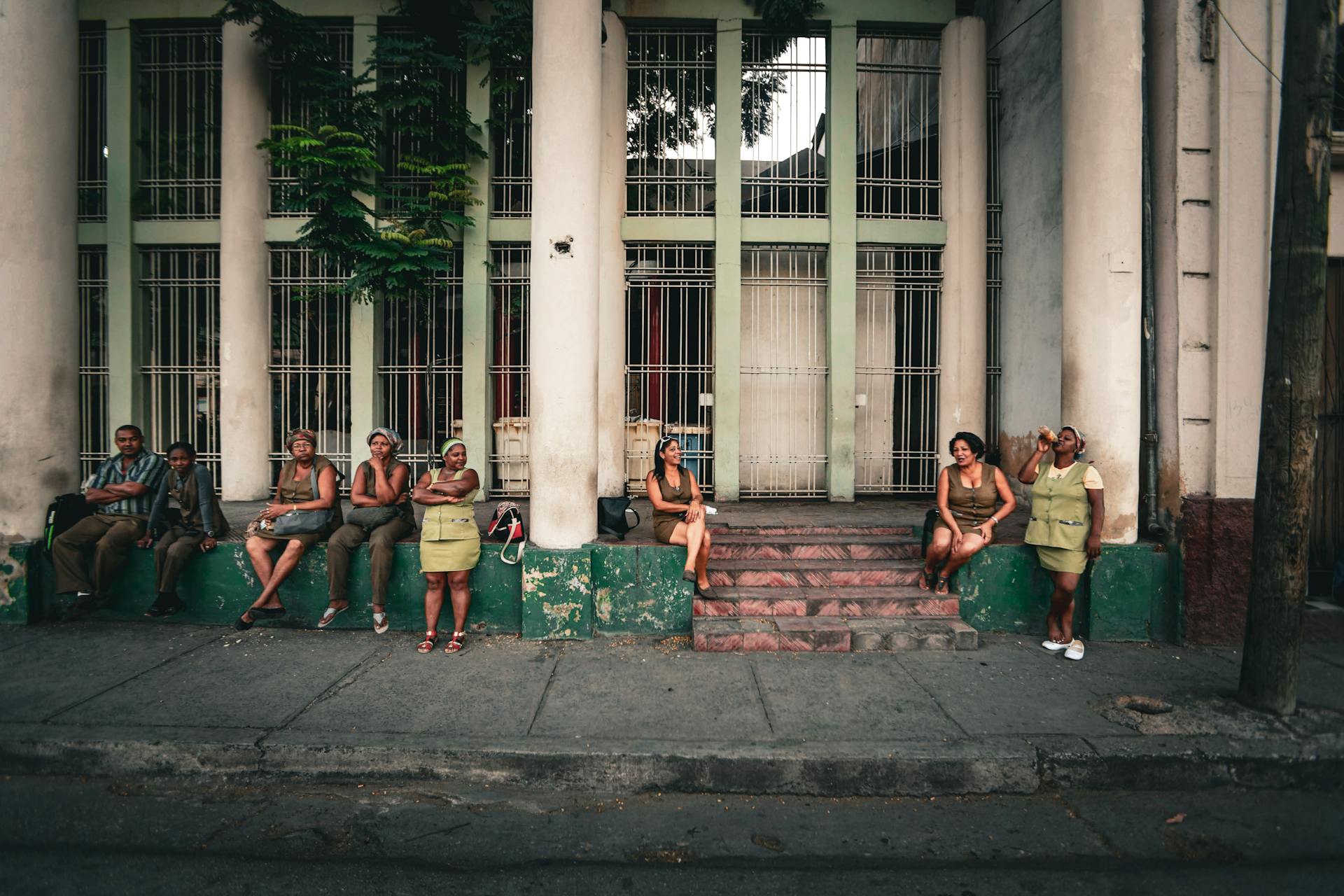 A diverse group of people resting on steps in front of a building on an urban street.