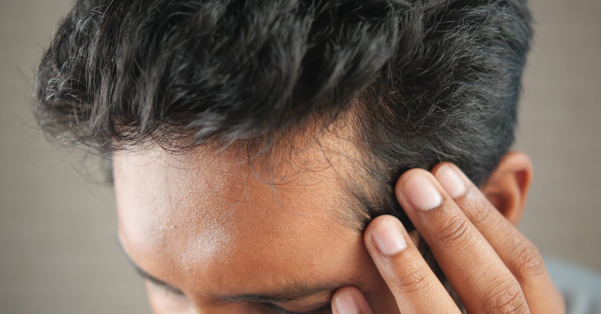 A man's hand touching his head in contemplation, neutral tones and soft lighting