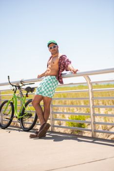 Man enjoying summer by the beach, leaning on railing with a bicycle nearby, in Long Beach, NY.