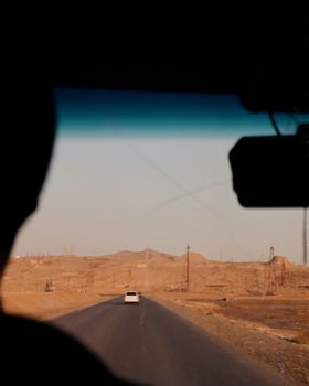 View from a car on a long empty road through a desert landscape under a clear sky.