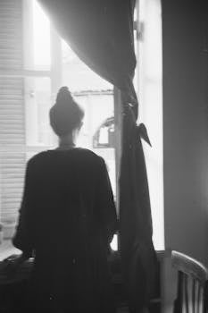 A silhouetted woman stands by a window with natural light filtering in.