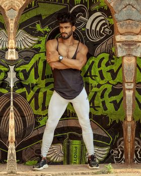 Confident man in fitness attire poses in front of a vibrant graffiti wall. Urban fashion meets art.