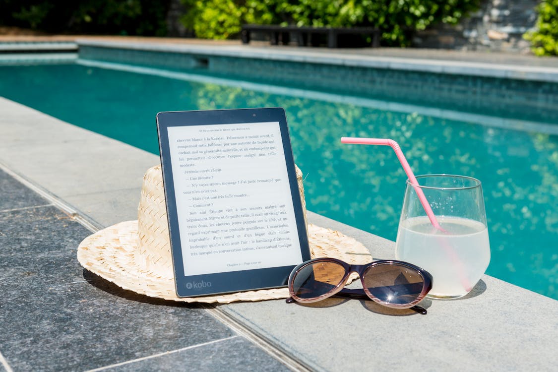 Free Black Kobo Table, Sunglasses, and a Glass of juice at Pool Edge Stock Photo