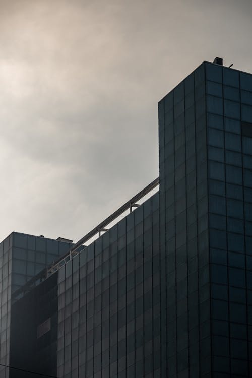 Free A low-angle shot of a modern glass building under a gloomy sky. Stock Photo