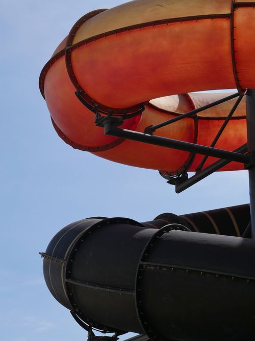 Free Bright orange and black waterslide twists against a vivid blue sky, capturing playful summer fun. Stock Photo