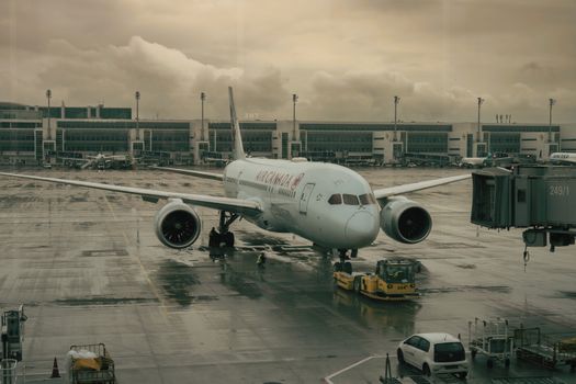 An airplane parked on a wet tarmac at Munich Airport under cloudy skies.