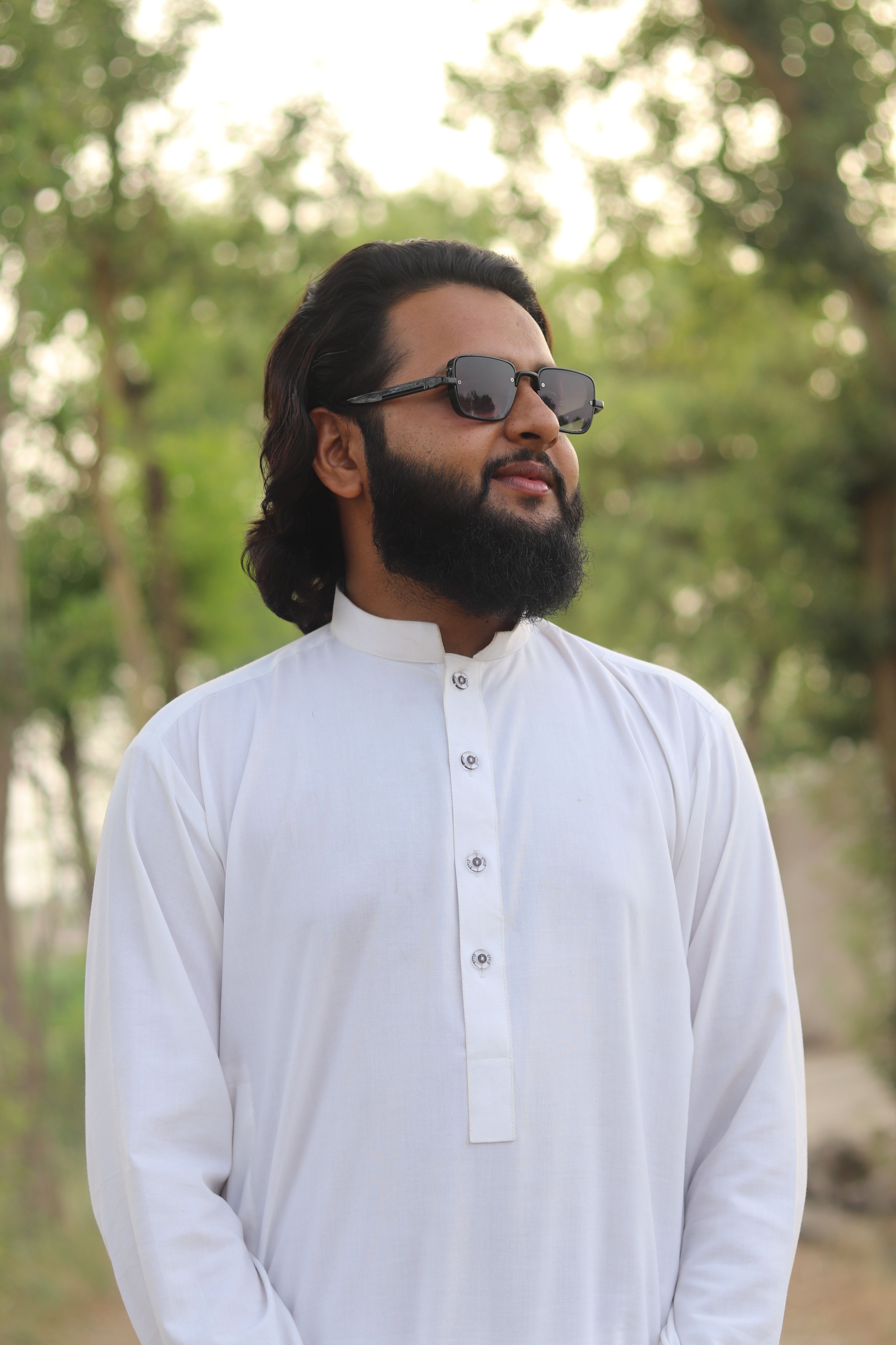 Portrait of a bearded man wearing sunglasses and a traditional white kurta in an outdoor setting.