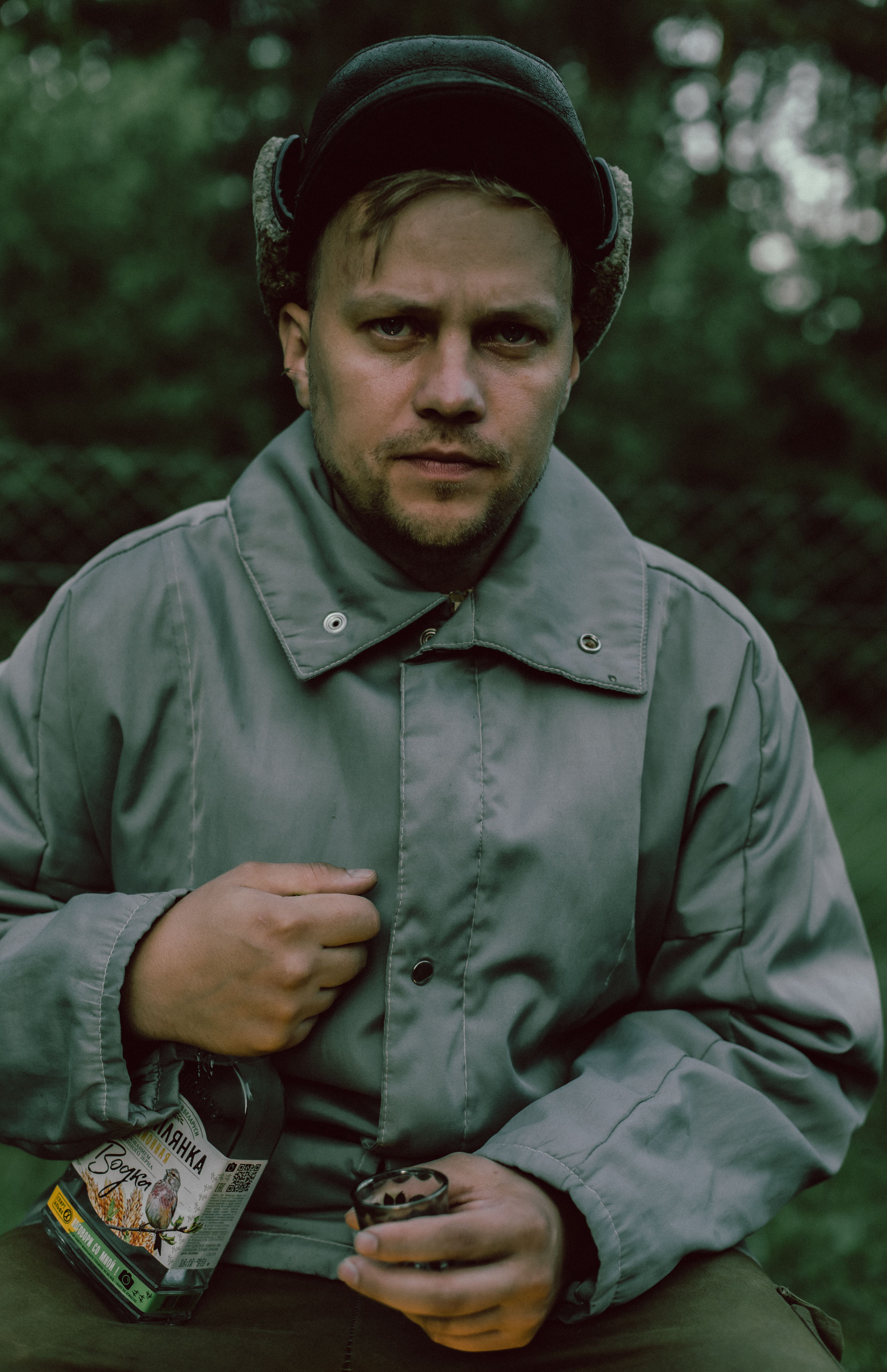 A man in a coat holding a bottle and shot glass outdoors.
