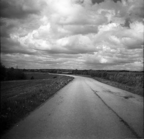 Grayscale Photo of Road Under Cloudy Sky