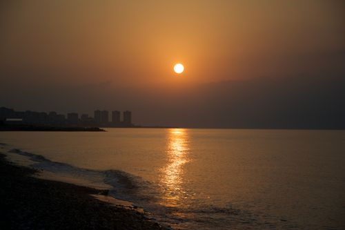 Free Peaceful sunset over the ocean with a distant city silhouette creating a serene view. Stock Photo