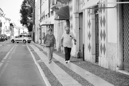Elderly couple strolling along a sidewalk in Villafranca di Verona, Italy.