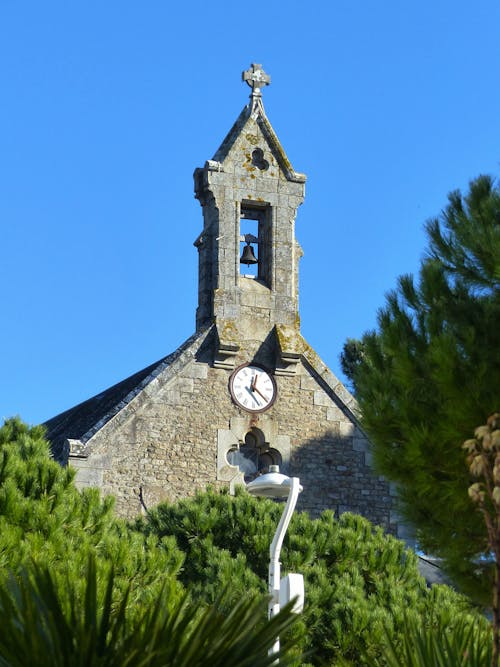 View of a Church Bell Tower and a Clock on the Facade under Blue Sky 