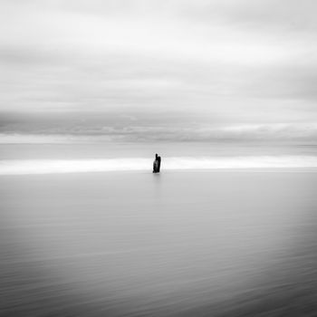 Calm and minimalist black and white seascape with cloudy sky and a distant horizon.