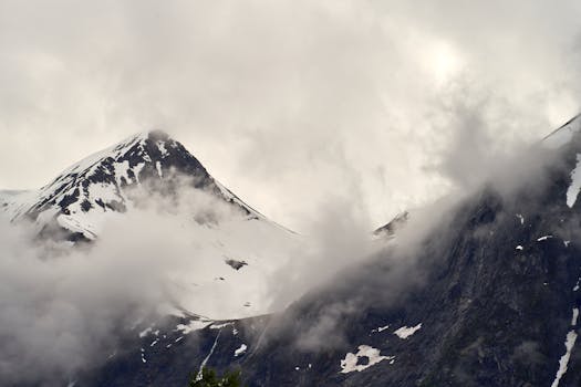 Majestic view of a snow-covered alpine mountain enveloped in fog and mist.