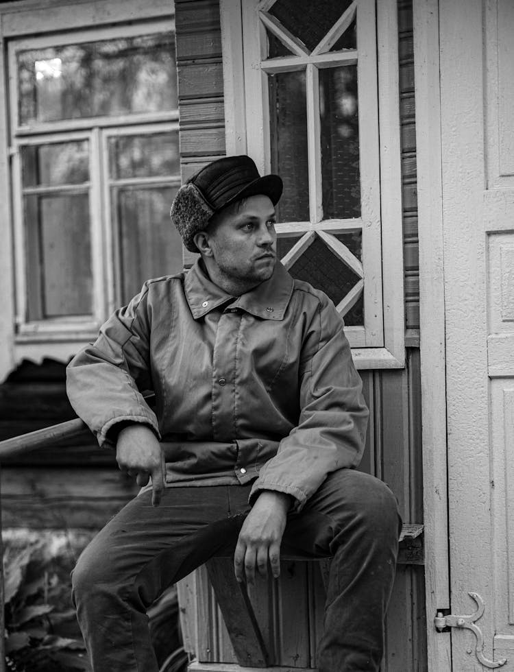 A Man Sitting In Front Of A House 