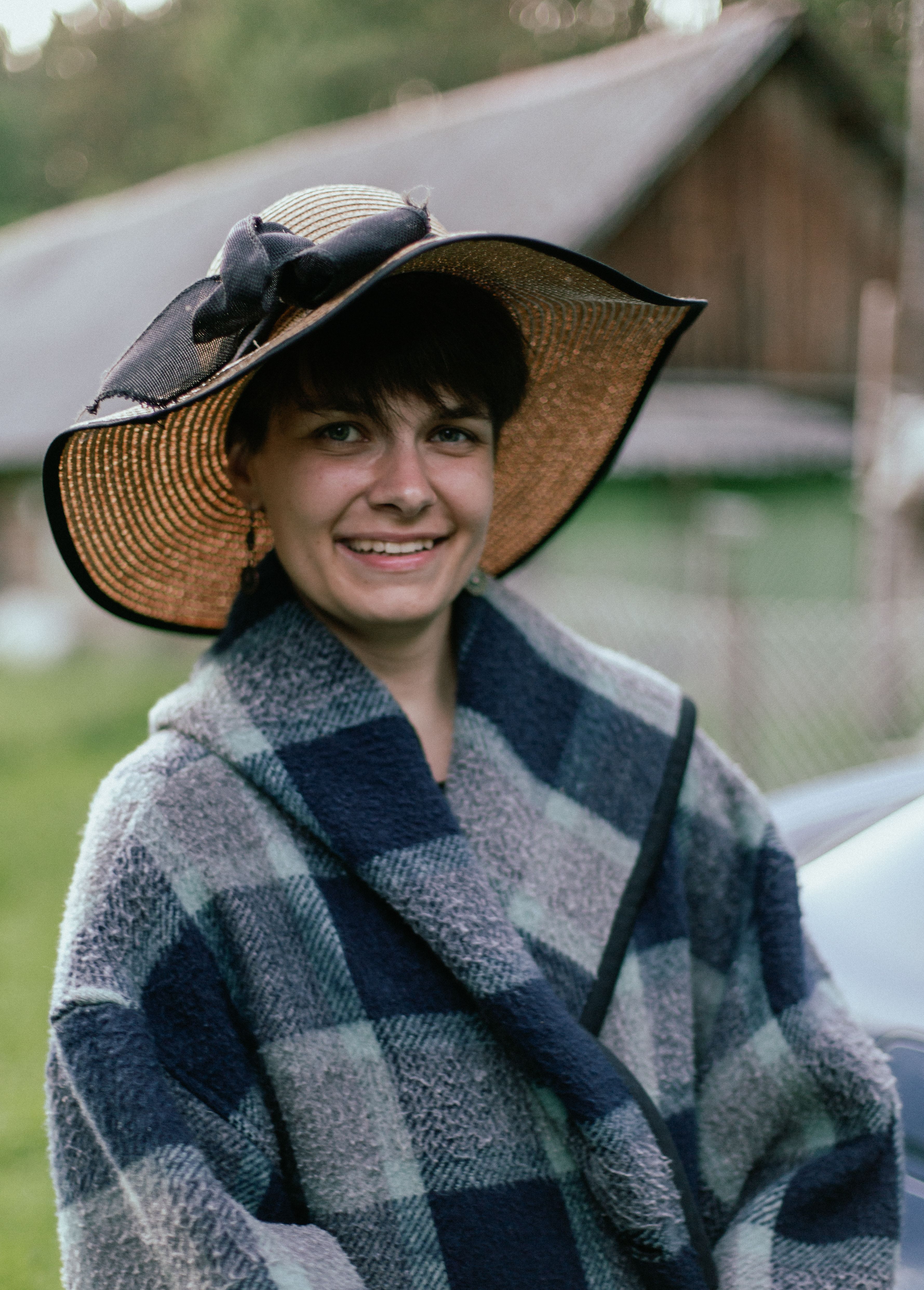 Smiling woman wearing a stylish hat and checkered coat outdoors, exuding warmth and charm.