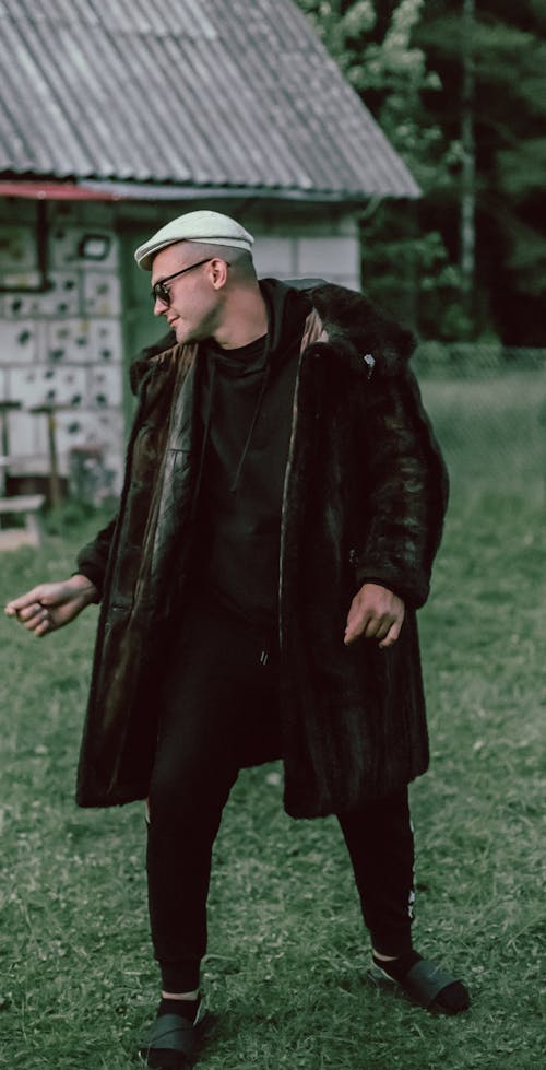 A Man in Flat Cap Wearing Trench Coat while Standing on Grass Field