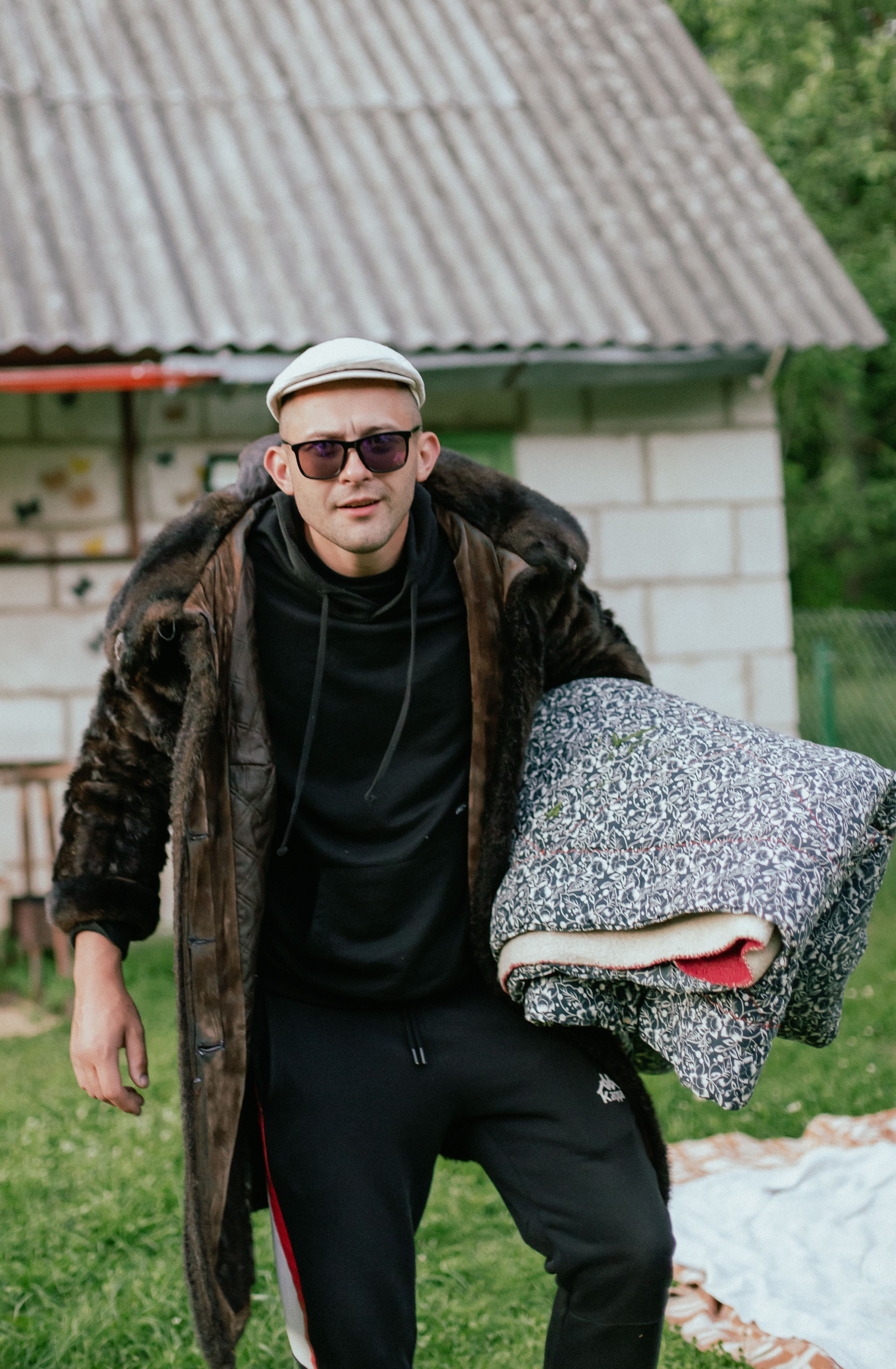 Caucasian man in a stylish outfit holding a blanket, standing in a backyard setting.