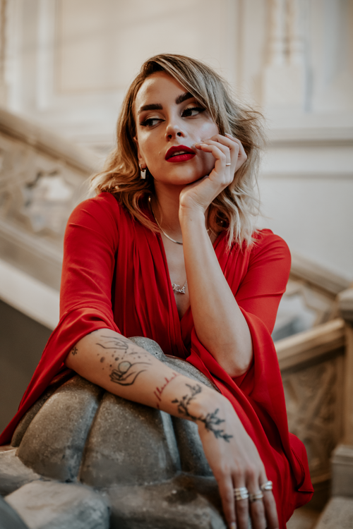 Free Stylish woman in a red dress, showcasing tattoos indoors, displaying elegance and confidence. Stock Photo
