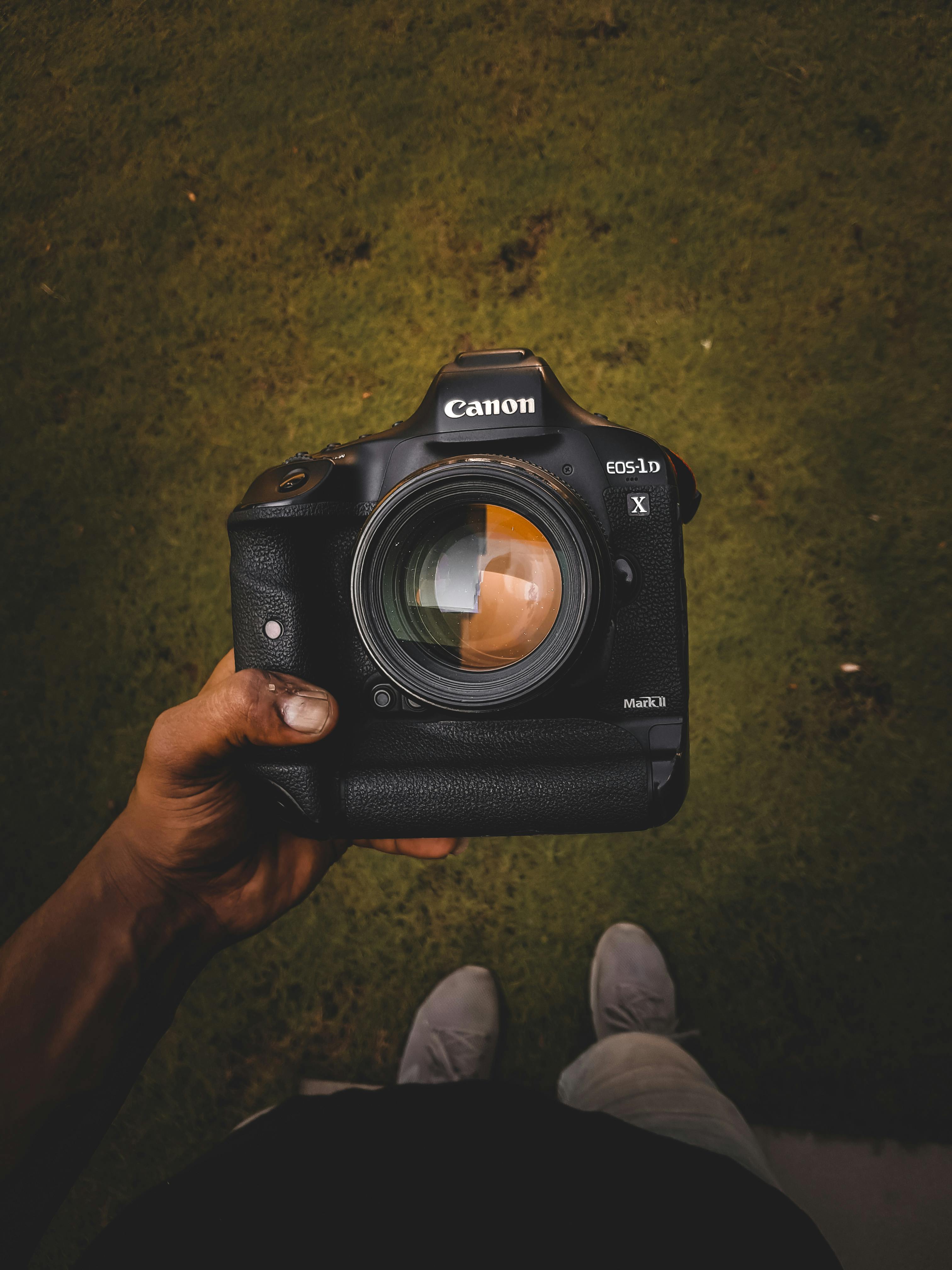 A close-up photo of a DSLR camera held by a person, taken in an outdoor setting.