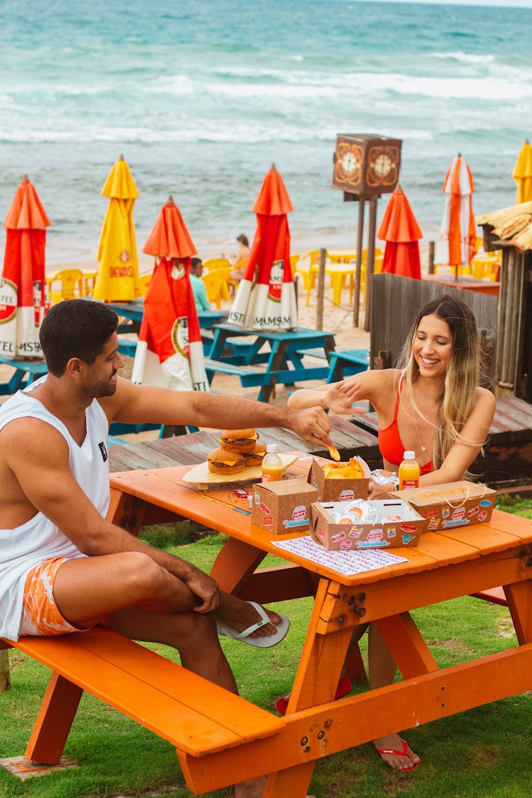 Man And Woman Sitting And Eating In A Restaurant Patio On A Seashore 