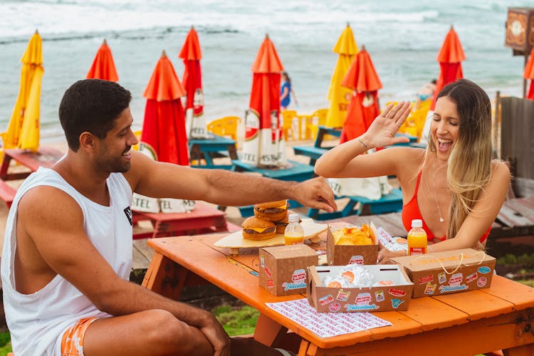 Man And Woman Sitting And Eating In A Restaurant Patio On A Seashore 