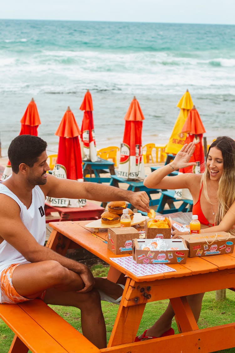 Man And Woman Sitting And Eating In A Restaurant Patio On A Seashore 