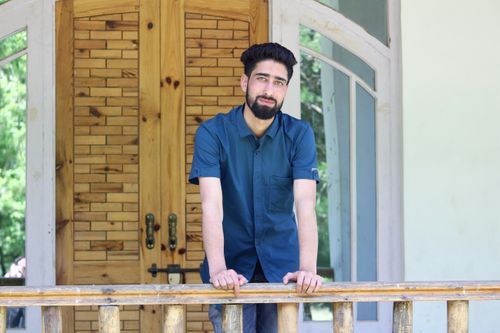 Free A man with a beard leaning on a wooden railing outdoors next to a wooden door. Stock Photo