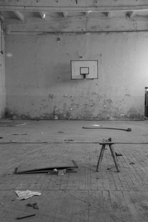 Free Black and white photo of a neglected indoor basketball court with peeling walls and scattered debris. Stock Photo