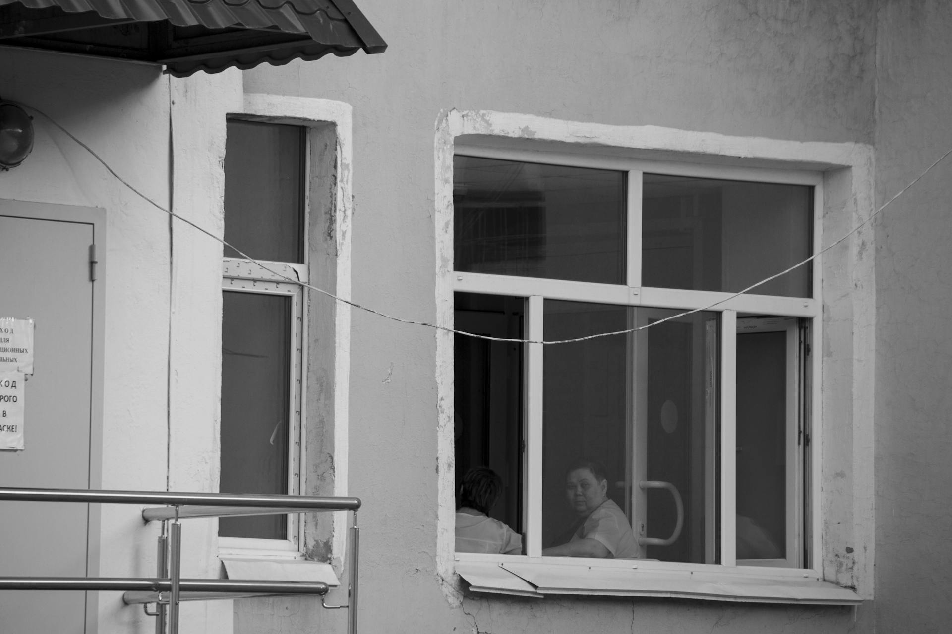 A person gazing through a window from inside a hospital building in black and white.