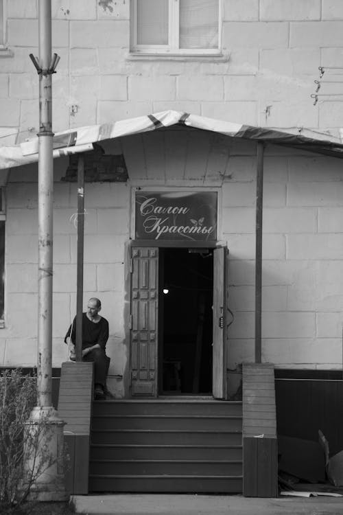 Grayscale Photo of a Man Sitting Near the Wooden Stairs 