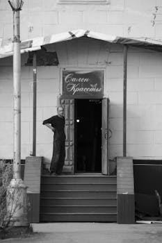 Man standing outside a beauty salon on stairs. Urban black and white shot.