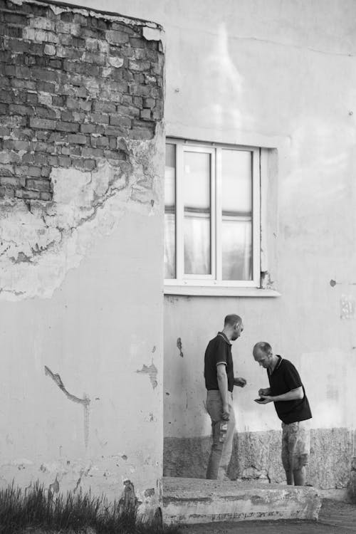 Black and White Photo of Two Men Standing under the Window of a Facade of a Building