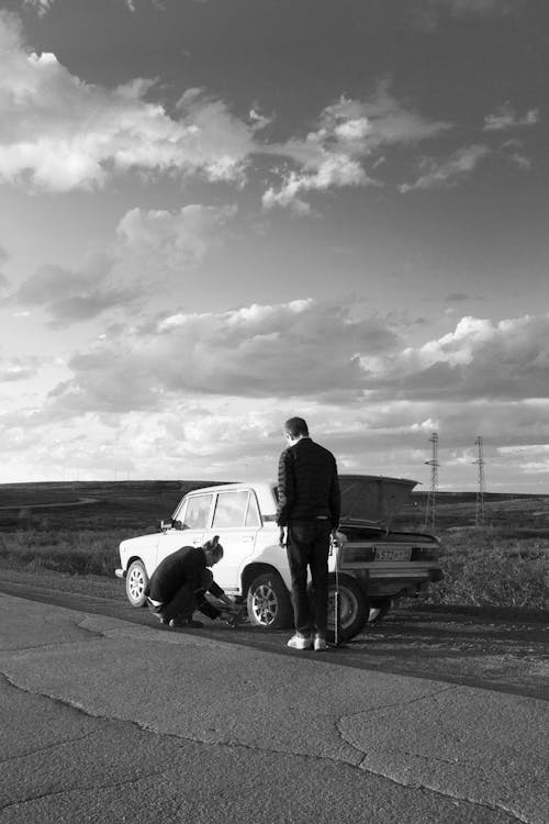 Free Grayscale Photo of Man in Black Jacket Standing Beside Car Stock Photo