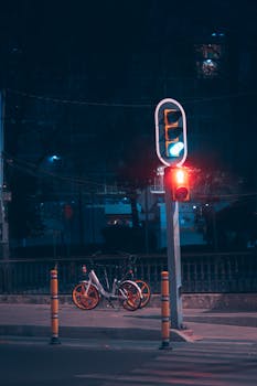 A parked bicycle under illuminated traffic lights at a quiet night street crossing.