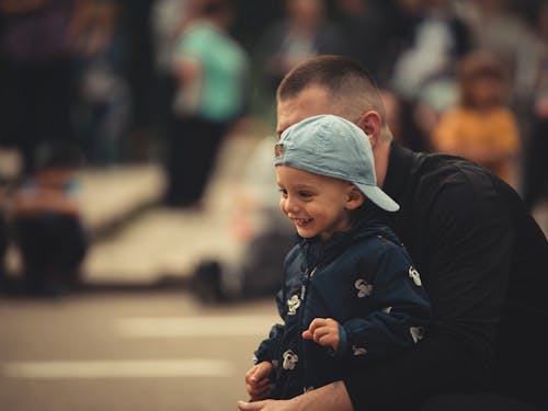 A Boy in Blue Cap Standing Beside His Father while Looking Afar