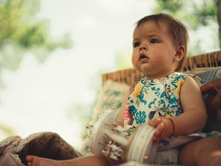 A Cute Little Baby Sitting While Holding A Toy