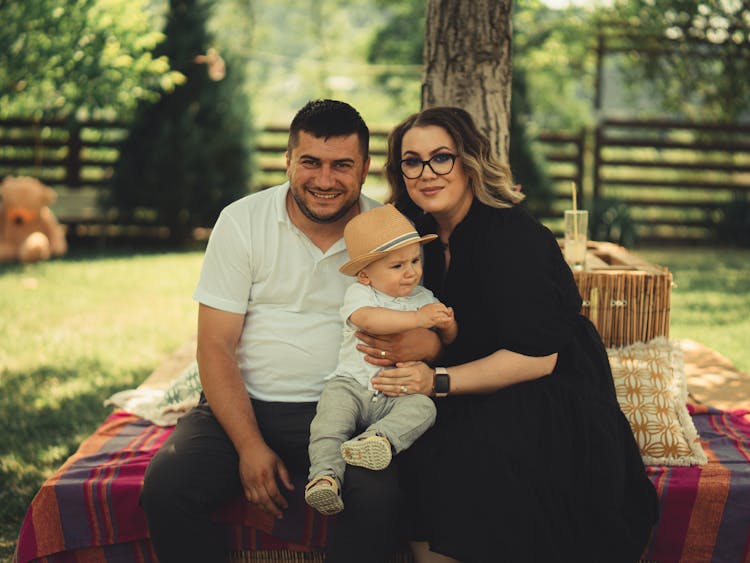 Photo Of A Father, A Mother, A Son Witting On Blanket In The Garden