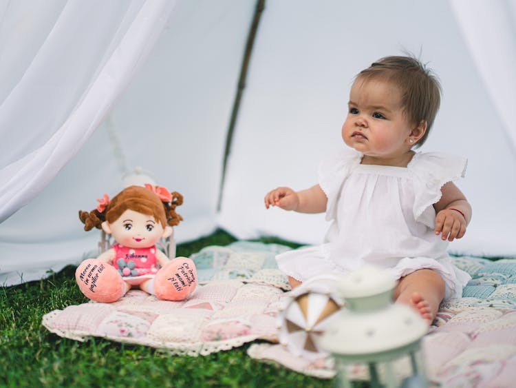 Baby Girl With A Doll Sitting In A White Tent