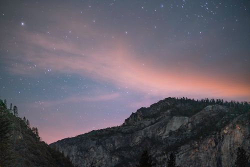 Free A serene view of a starlit night sky over a rugged mountain landscape. Stock Photo