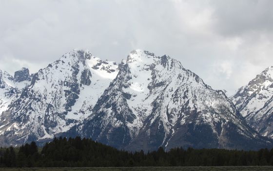 Majestic snowcapped mountains with lush greenery below under a cloudy sky.