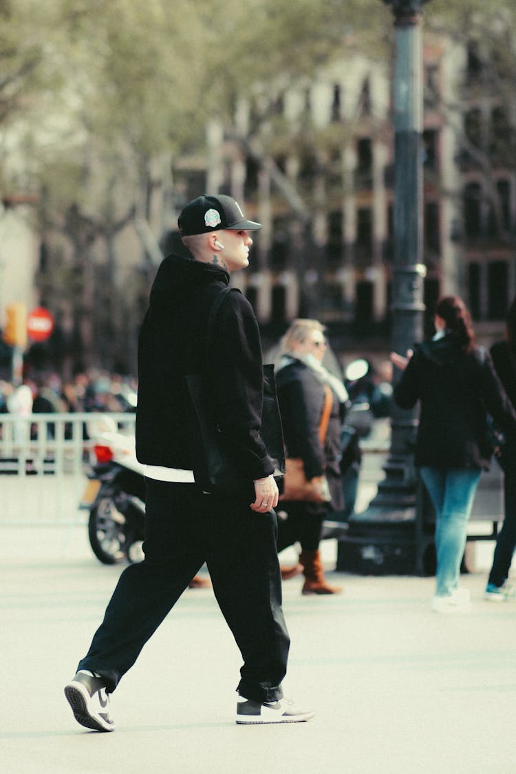 A Man In Black Jacket And Black Pants Walking On The Street