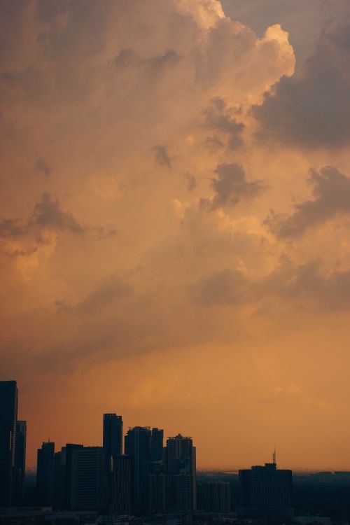 Free Silhouette of a city skyline under dramatic orange sunset clouds, creating a moody atmosphere. Stock Photo